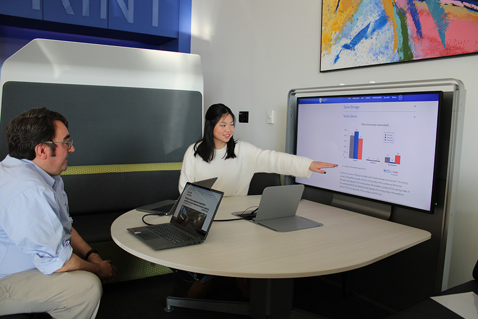 Klasen and Rogers reviewing data from the latest SLU/YouGov Poll in the Academic Tech Commons in Pius XII Memorial Library. Klasen gestures toward a screen with bar graphs while Rogers looks on.