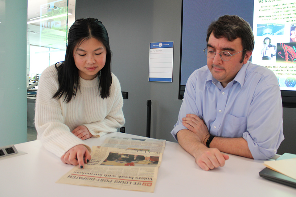 Klasen and Rogers read a story in the St. Louis Post-Dispatch about the SLU/YouGov Poll results. Klasen and Rogers sit at a table with a newspaper in front of them.