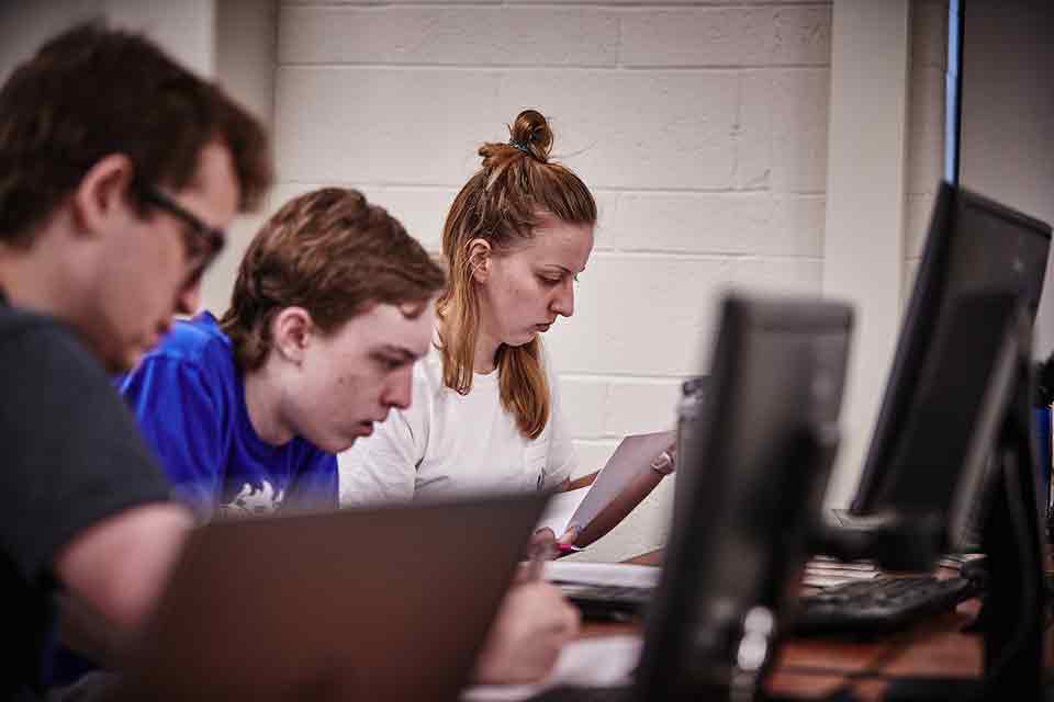 Computer Science faculty Computer Science students code on laptops in a classroom of the ISS building.