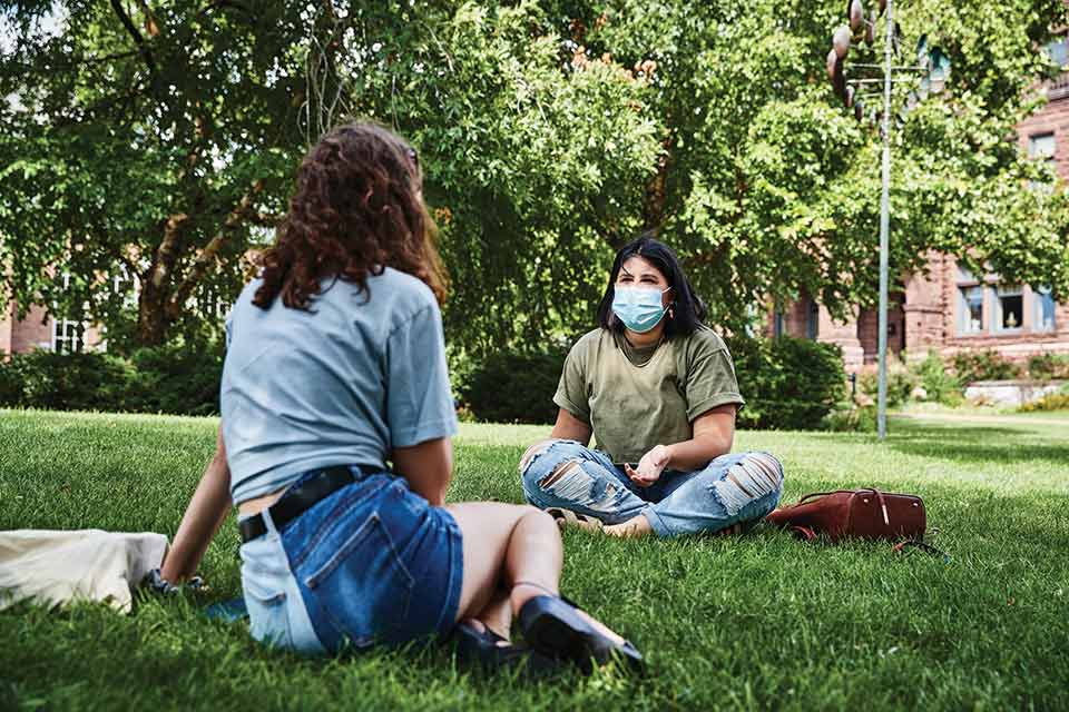 2020 Social Distancing Two female students sit and talk six feet apart on SLU's quad. They are both wearing medical masks.